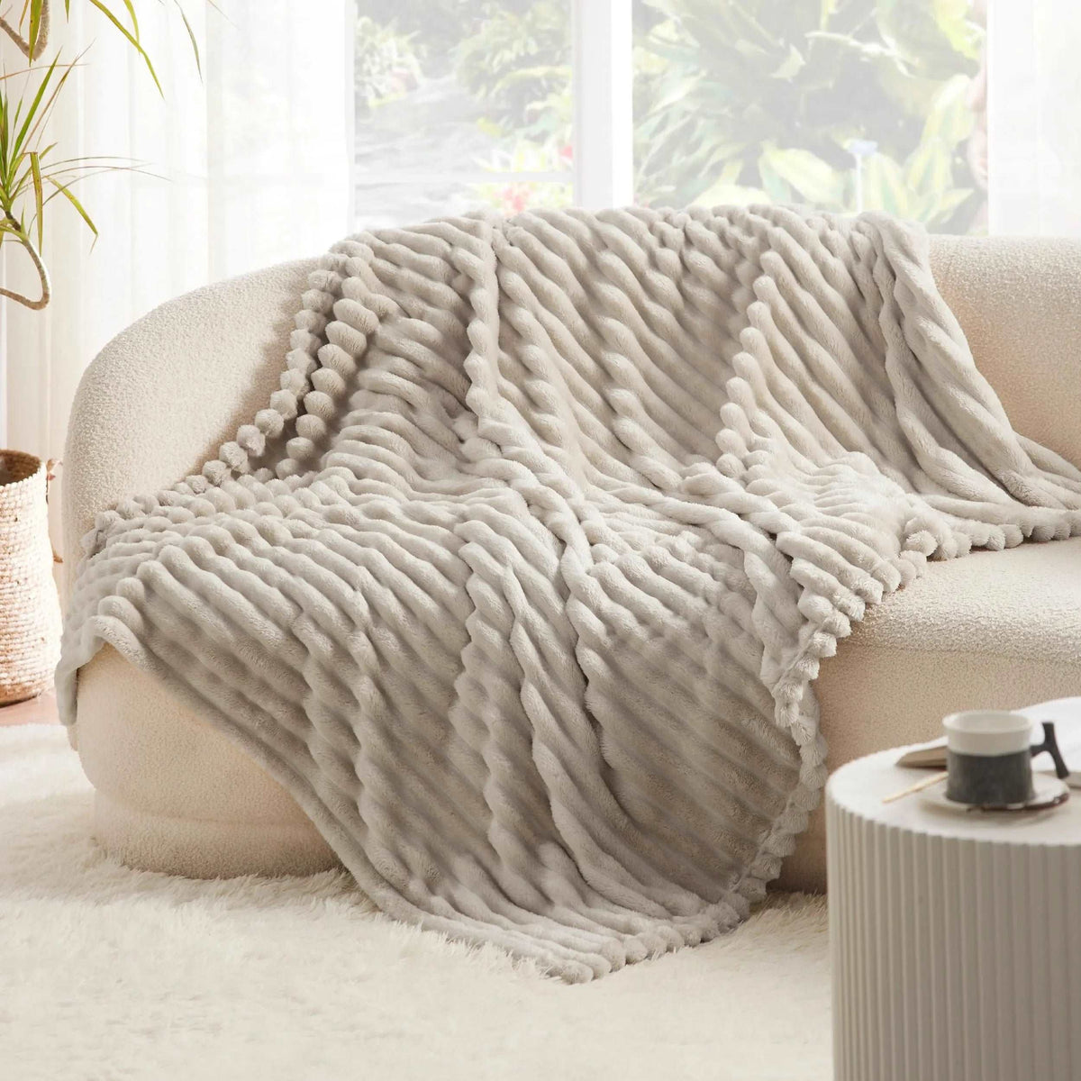 Beige faux rabbit fur throw draped over a curved cream sofa, its fluffy pleats catching the window light
