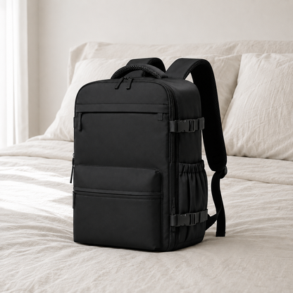 Black laptop backpack with vacuum compression chamber standing on a linen bed in a bright hotel bedroom