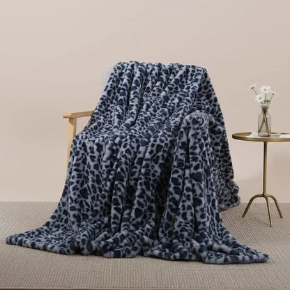 A blue leopard print throw blanket with navy spots on a blue-gray ground, thrown over a wooden armchair on a woven rug.