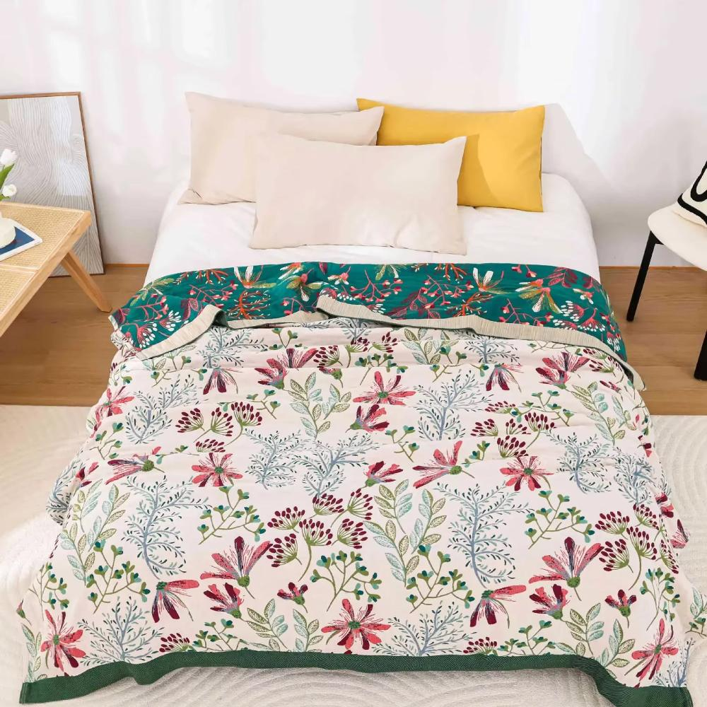 Cream wildflower gauze blanket spread over a bed, with the teal reverse folded back at the pillows and a dark green band along the foot
