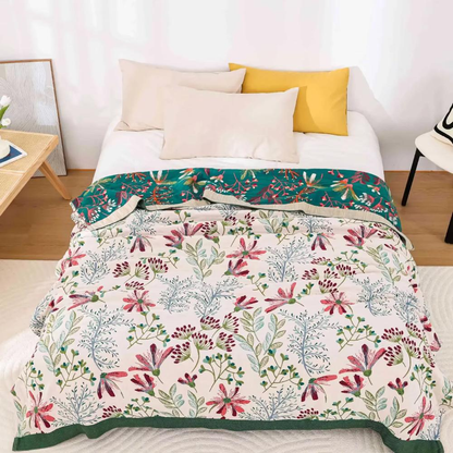 Cream wildflower gauze blanket spread over a bed, with the teal reverse folded back at the pillows and a dark green band along the foot