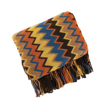 A chevron knit throw in orange, mustard, blue and dark brown, folded square on a white background with its tassel fringe hanging down.