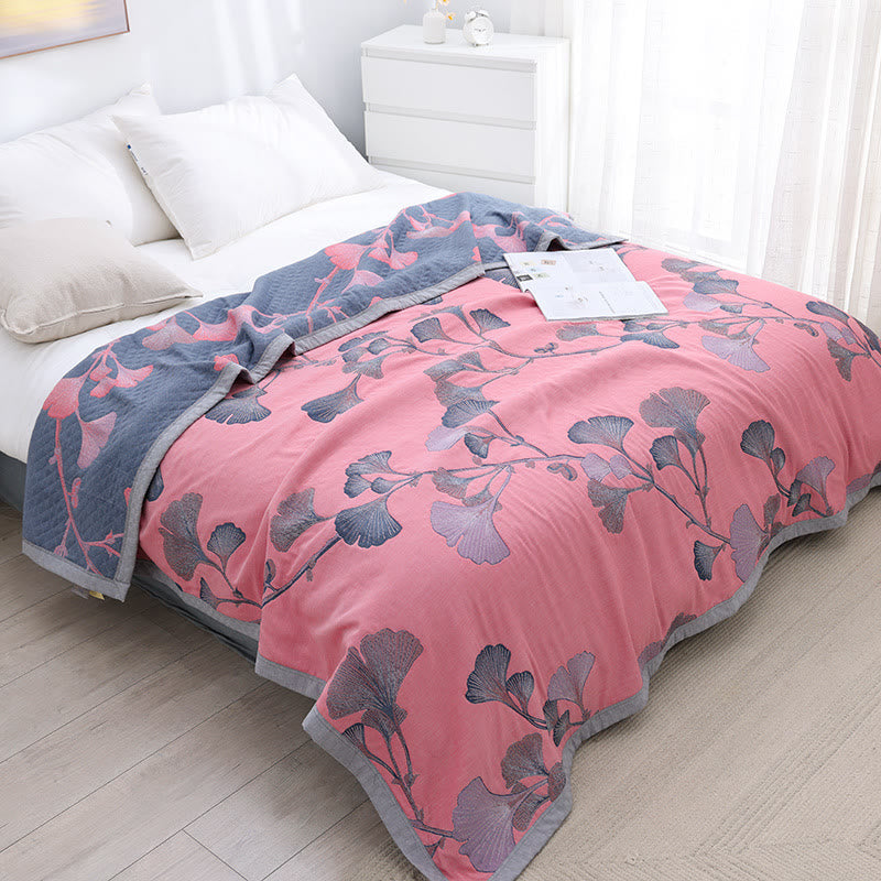 Pink ginkgo leaf gauze quilt spread over a bed, with its slate gray reverse and coral pink leaves folded back at the pillows