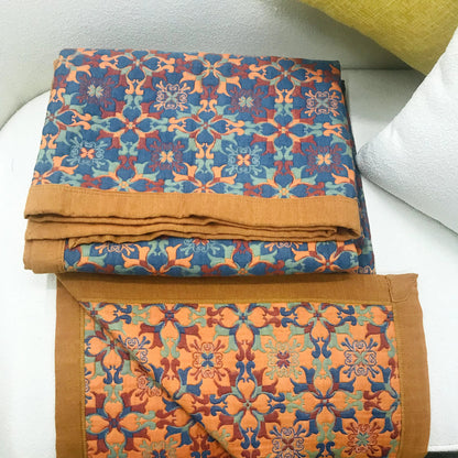 Orange and blue cotton quilt folded on a white bench, the blue patterned front on top and the orange reverse and wide orange border below