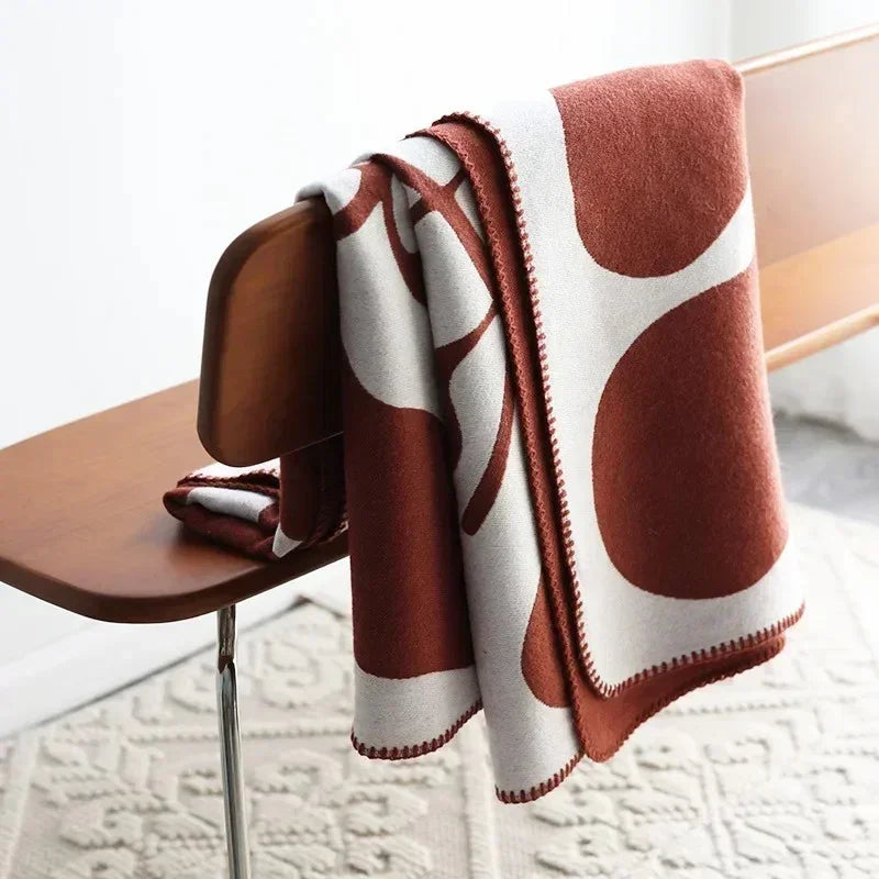 A rust and off-white knit throw blanket with an abstract pattern, folded and hung over the back of a wooden bench.