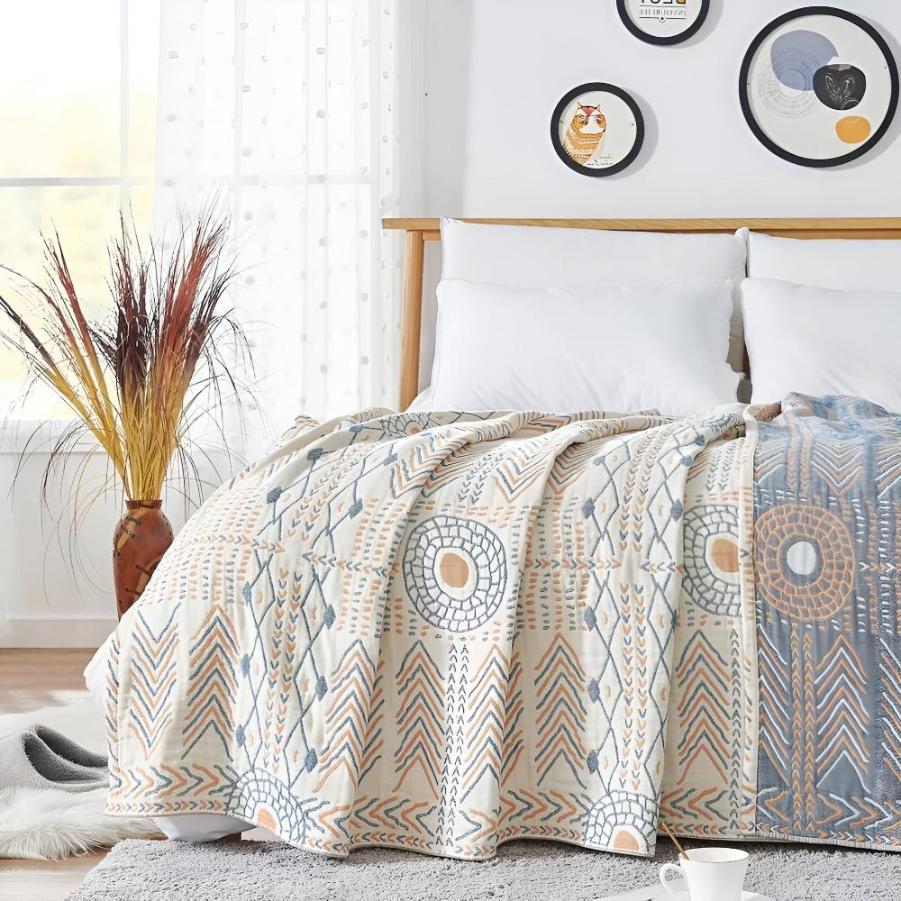 Reversible boho blanket spread over a bed, slate blue and orange sun rings and chevrons on cream, the blue reverse showing at one edge