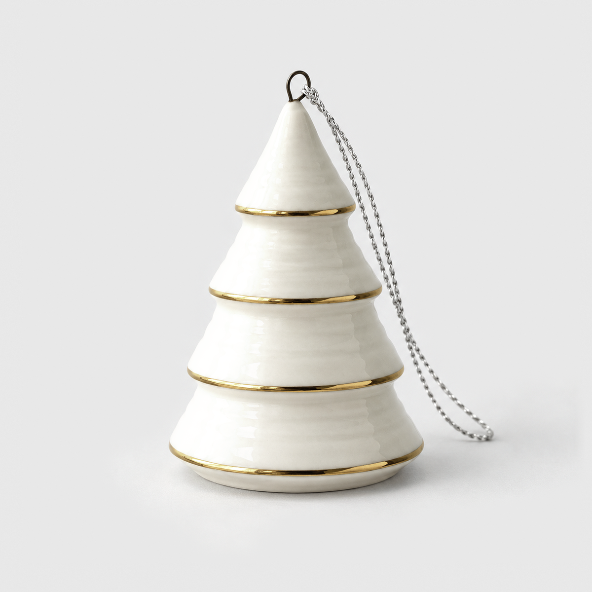 White ceramic Christmas tree ornament in the Cone style, a stepped cone with thin gold lines around each tier, standing on a light gray background with its silver hanging cord