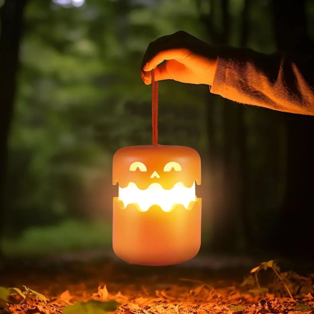 Orange pumpkin lantern lit and hanging from its cord in a hand, in woodland at dusk