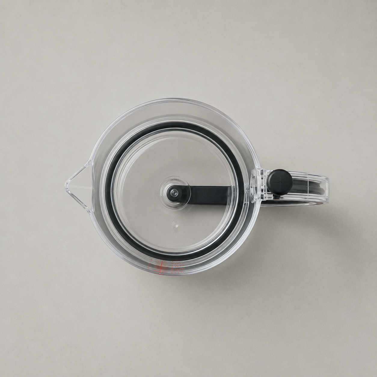Plan view looking straight down into the empty clear measuring cup on plain grey, the sealing plate filling the circle with its black seal ring, pour spout at the left and handle at the right