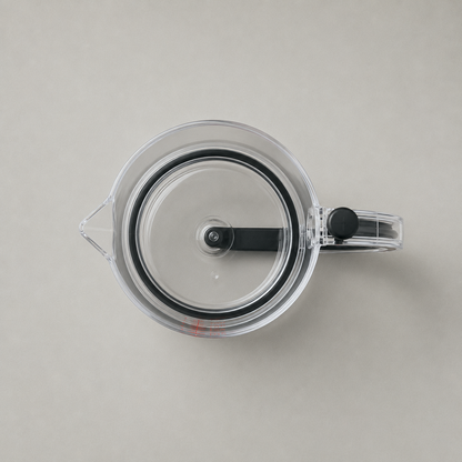 Plan view looking straight down into the empty clear measuring cup on plain grey, the sealing plate filling the circle with its black seal ring, pour spout at the left and handle at the right