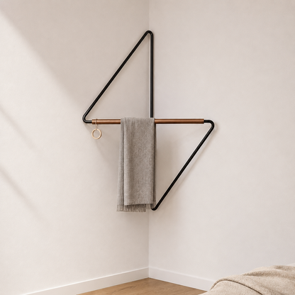 Black metal corner coat rack in a bedroom corner, a grey throw folded over the crossbar and the ring hanging empty at the left end.