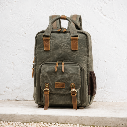 Army green waxed canvas camera backpack against a whitewashed courtyard wall.