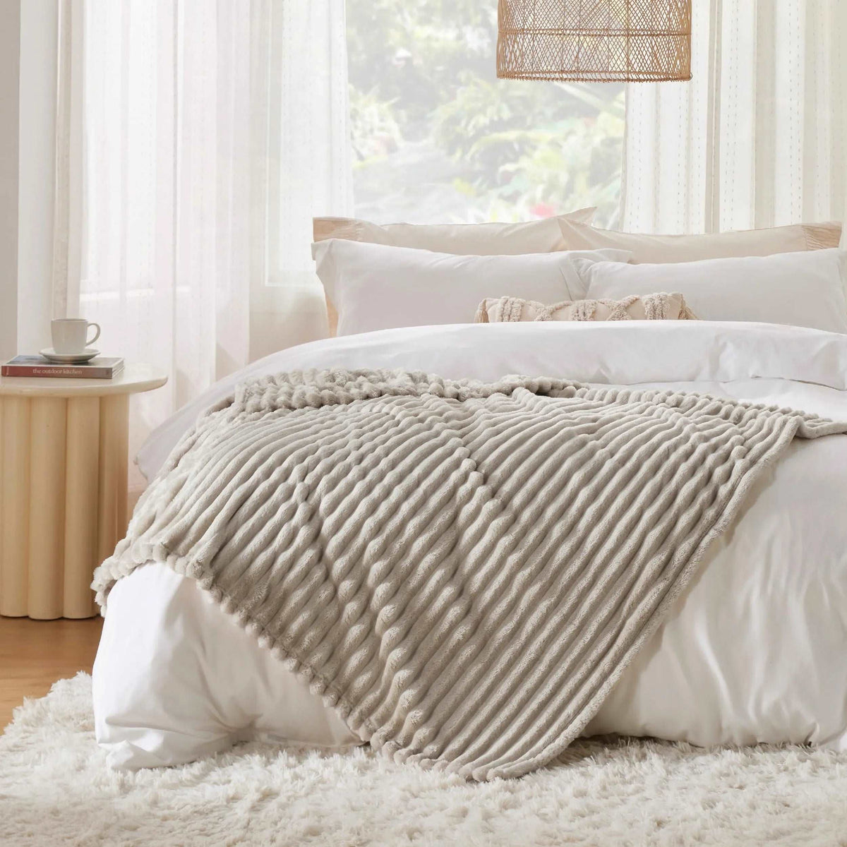 Beige pleated faux fur throw draped diagonally across a white bed in a bright bedroom