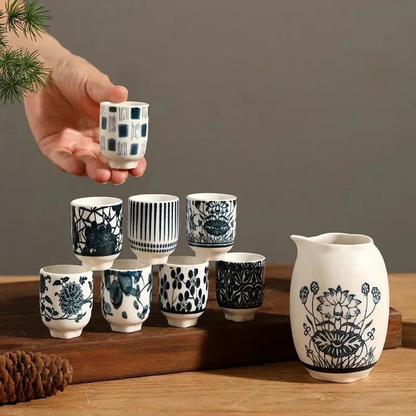 Eight blue and white sake cups stacked in a pyramid on a walnut board, the lotus decanter standing beside them.