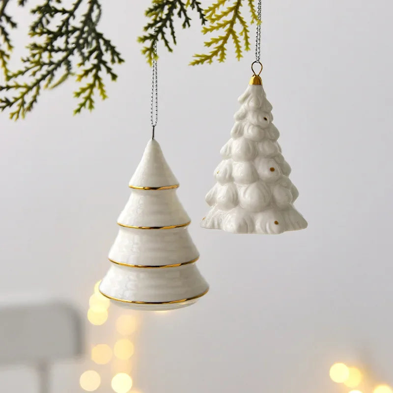 Cone and Frosted white ceramic tree ornaments hanging from a green sprig in front of a pale gray wall with warm lights behind
