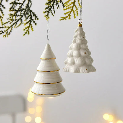 Cone and Frosted white ceramic tree ornaments hanging from a green sprig in front of a pale gray wall with warm lights behind