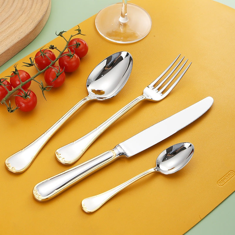 Mirror-polished flatware with gold-trimmed scroll handles laid on a yellow table mat