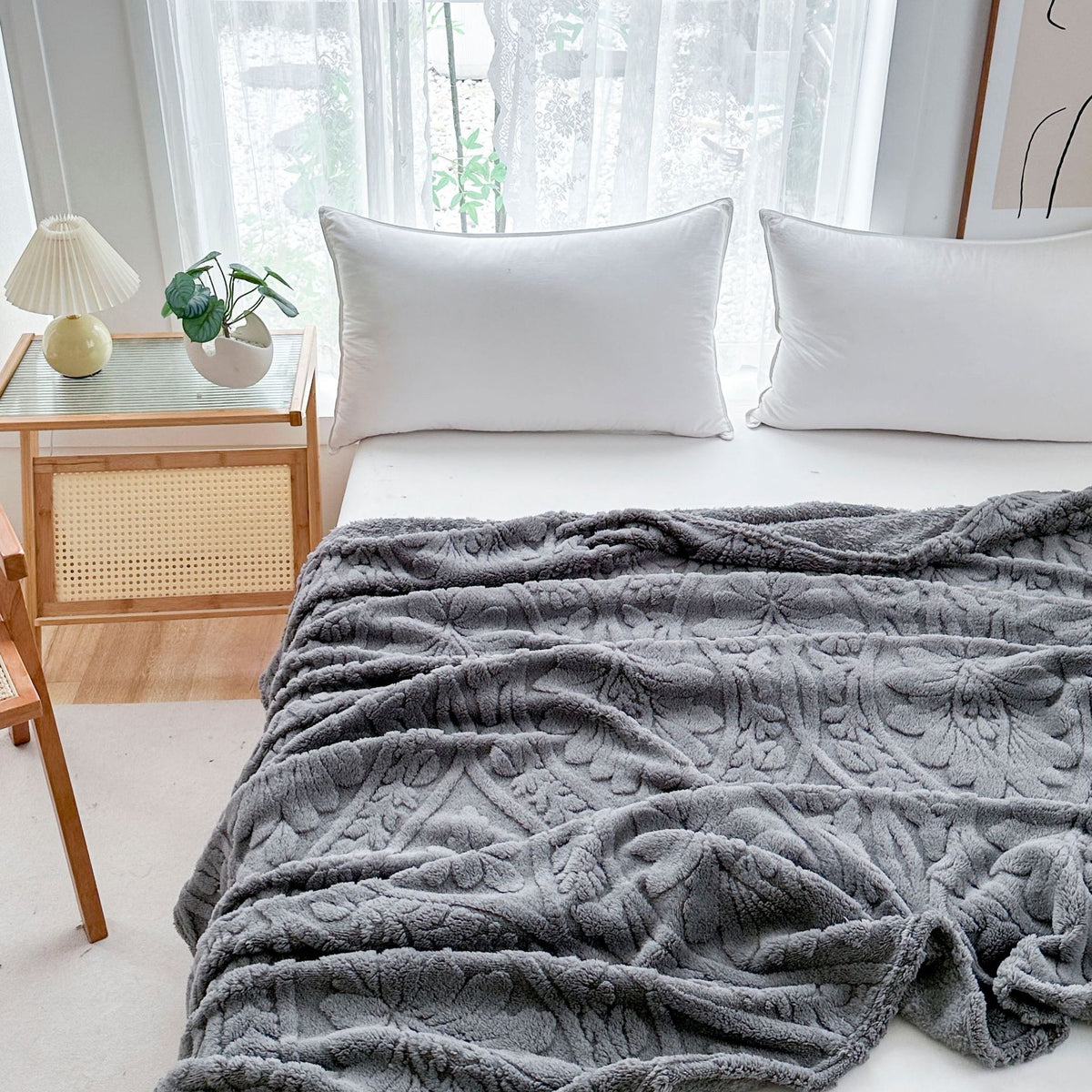 Gray fleece blanket loosely spread across a bed, its raised leaf and flower pattern up close