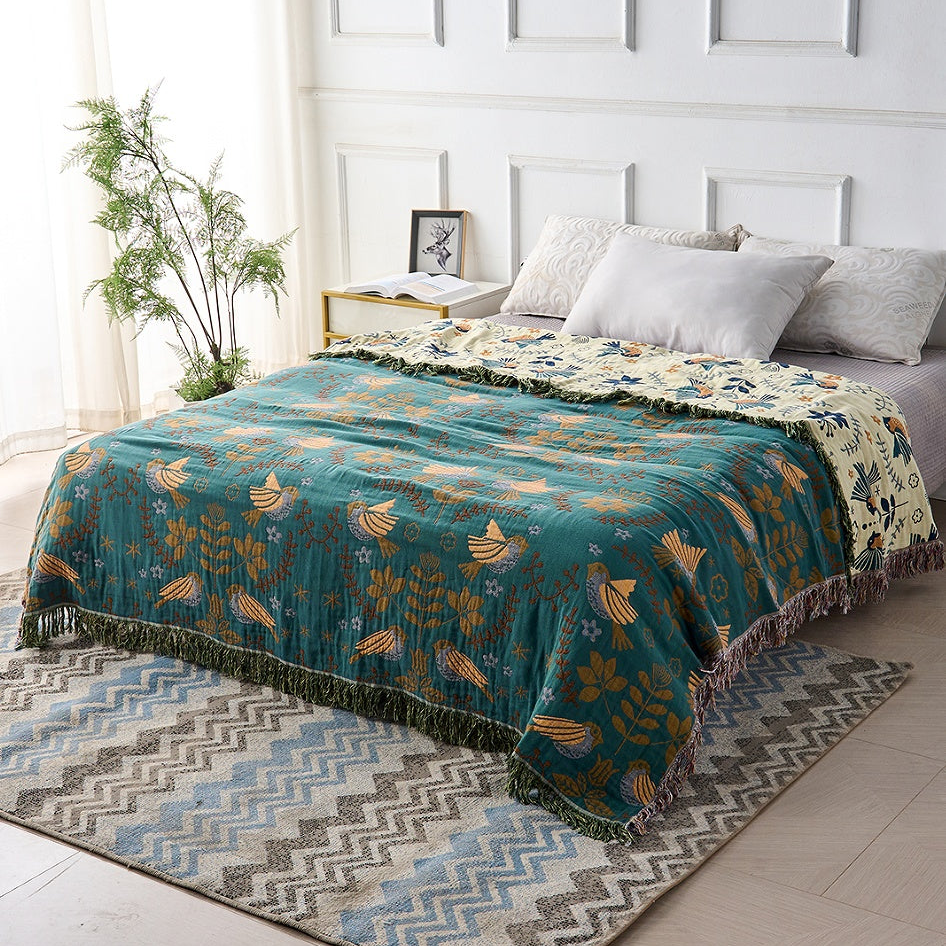 The bird throw spread across a made bed teal side up, with the cream side folded back at the pillows and down the right edge