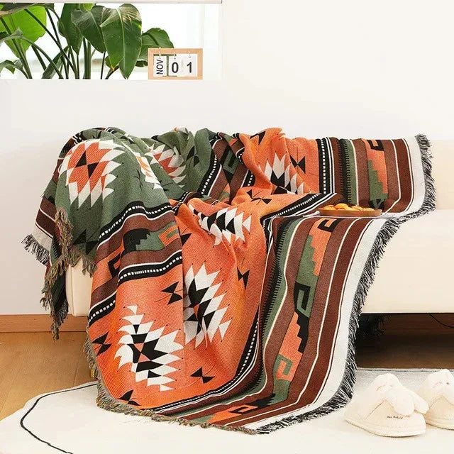 An orange jacquard throw with an olive band and black and white medallions, thrown over a cream couch with fringe at the ends