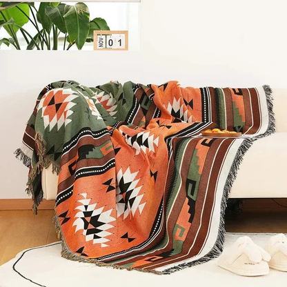An orange jacquard throw with an olive band and black and white medallions, thrown over a cream couch with fringe at the ends