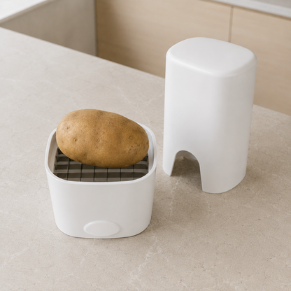 A whole raw potato resting on the stainless steel blade grid, with the press standing separately behind