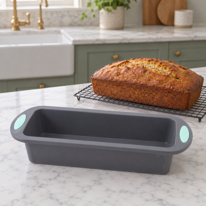 Gray silicone loaf pan on a marble worktop beside a whole banana bread on a cooling rack in a sage green kitchen