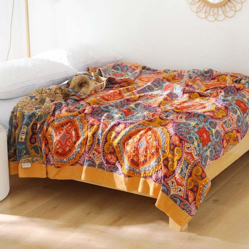 Boho paisley throw blanket spread over a low bed, large orange medallions and a mustard border