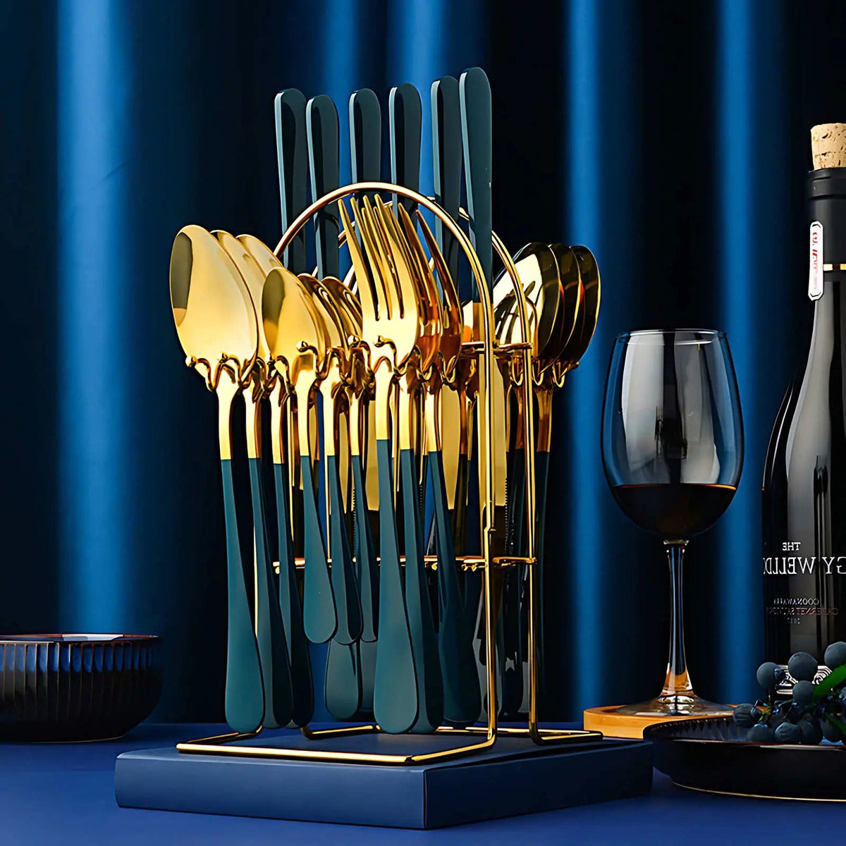 Teal and gold cutlery set on its arched gold rack beside a glass of red wine against a blue curtain