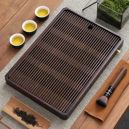 Slatted bamboo tea tray on a linen runner seen from above, three cups of tea beside it and a brush on a tan cloth.