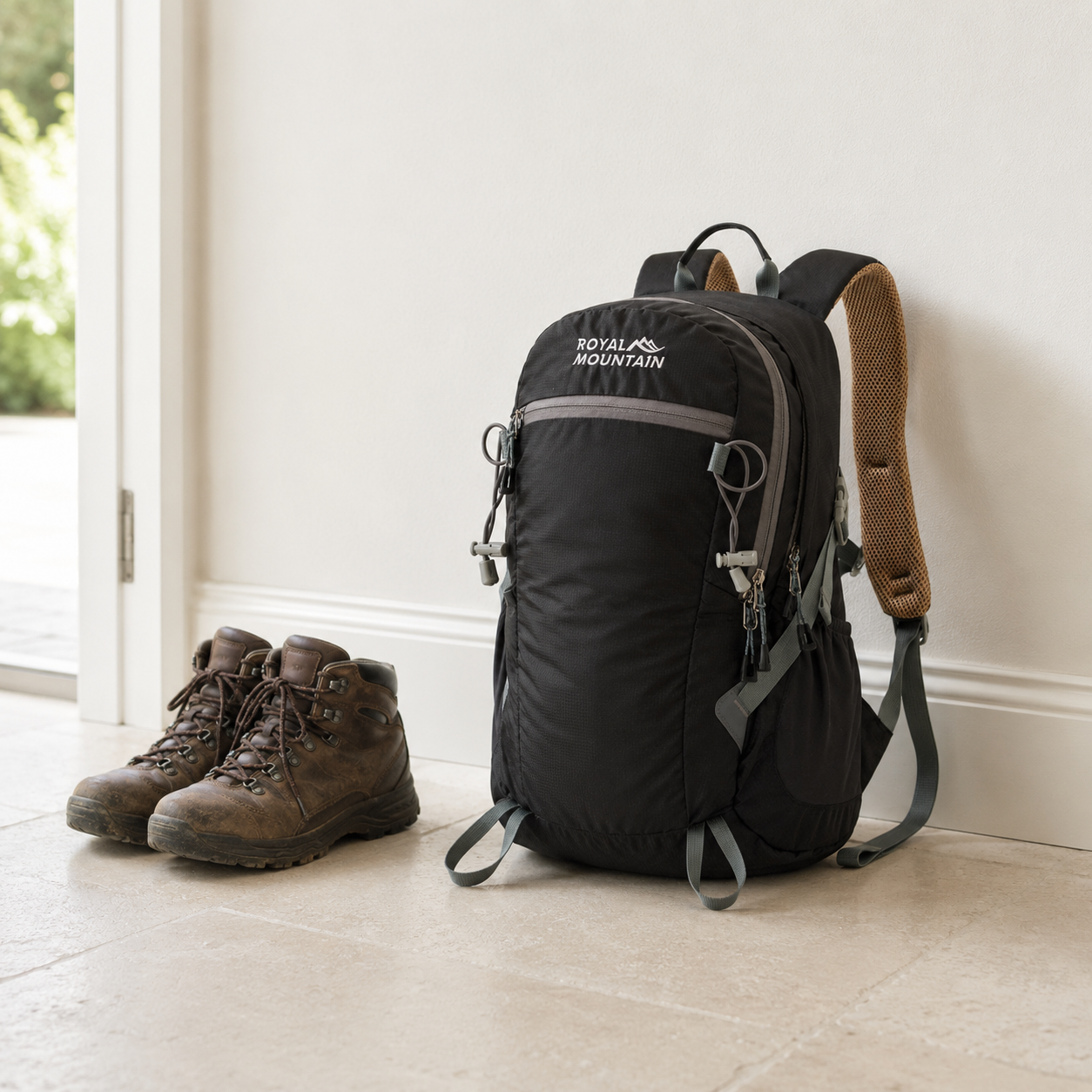 Black 30L hiking day pack standing on a limestone floor in a bright entrance hall beside a pair of walking boots