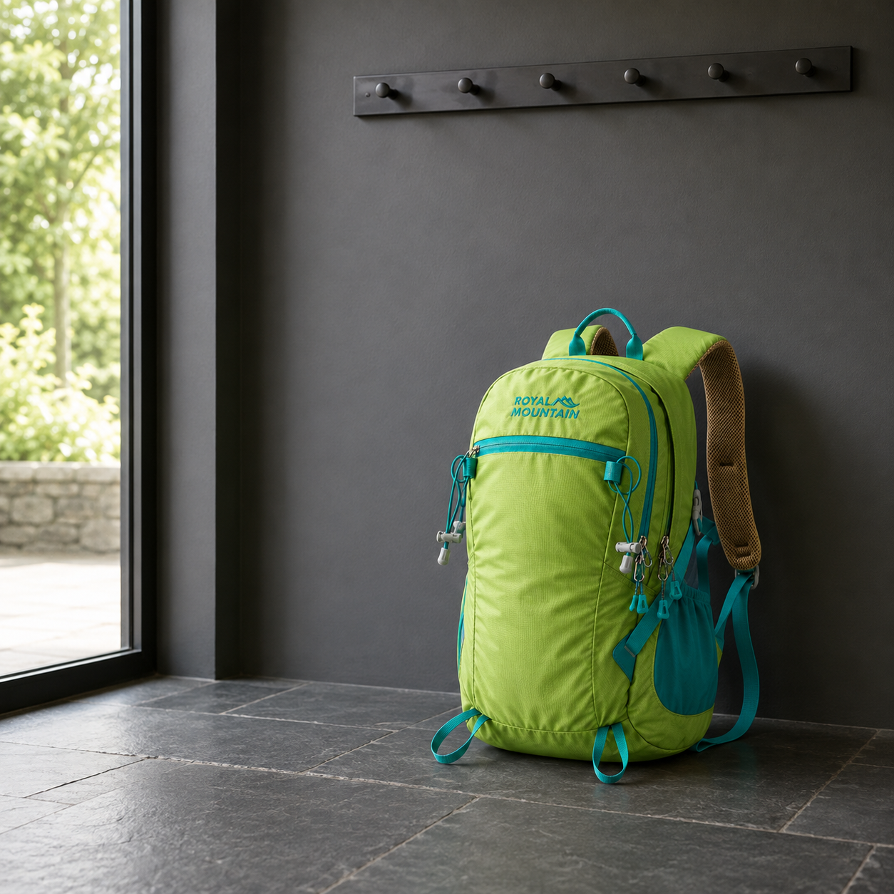 Green 30L hiking day pack with teal trim standing on a slate floor in a boot room below a row of coat hooks