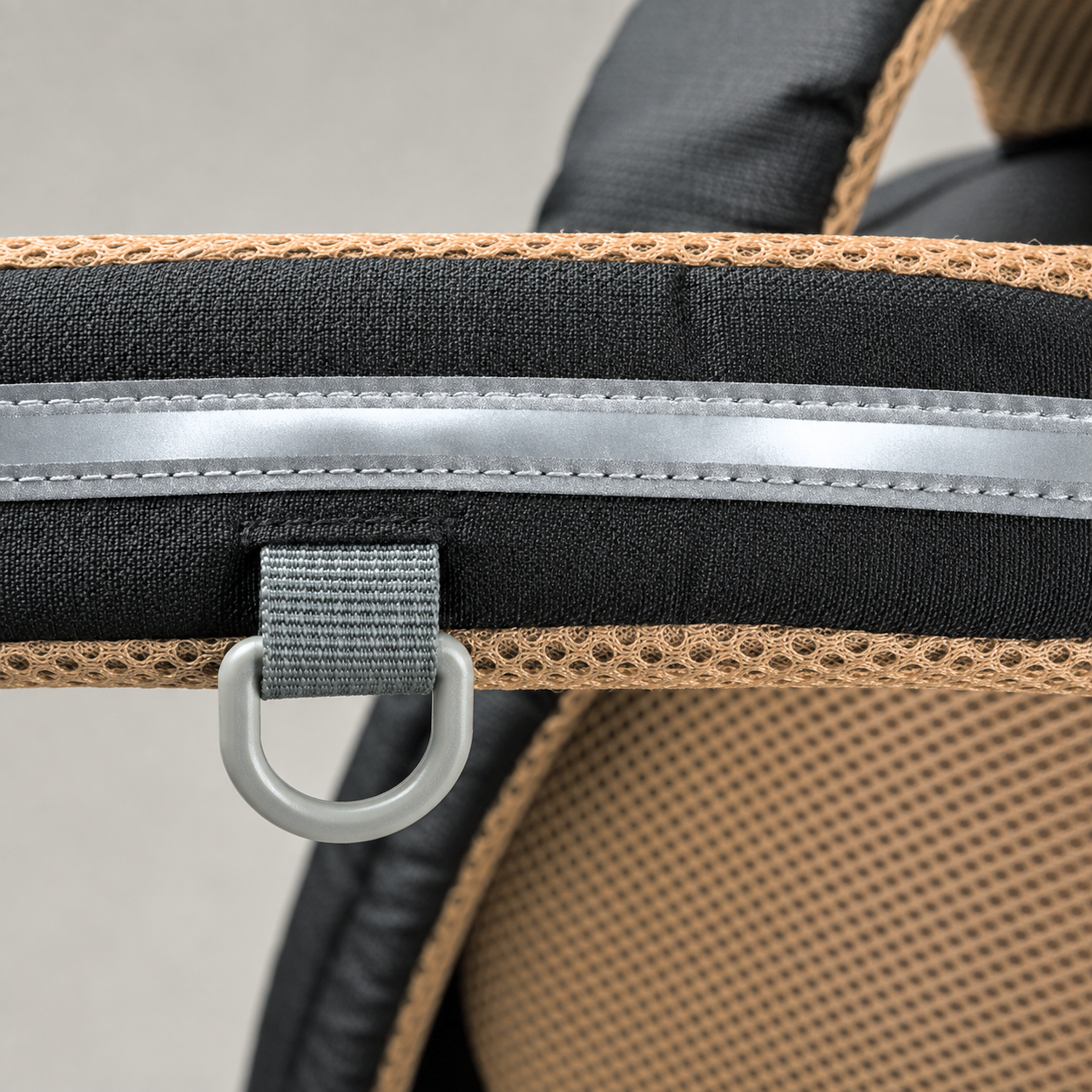Close view of a shoulder strap showing the silver reflective strip, the tan mesh inner face and the grey D-ring