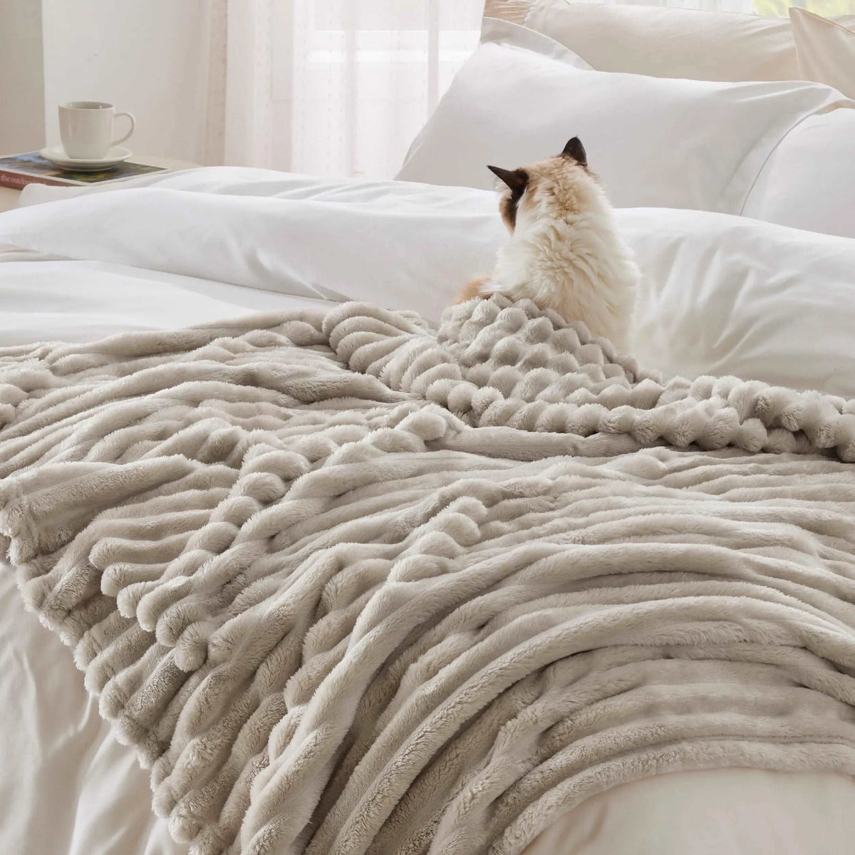 Beige faux rabbit fur throw bunched over a white bed, a cat sitting on its gathered pleats