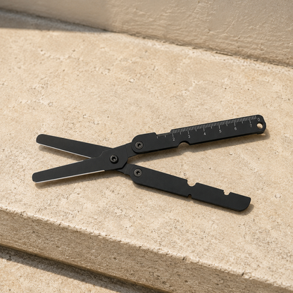 Black folding pocket scissors open on a pale limestone step, blades and handles both finished black.