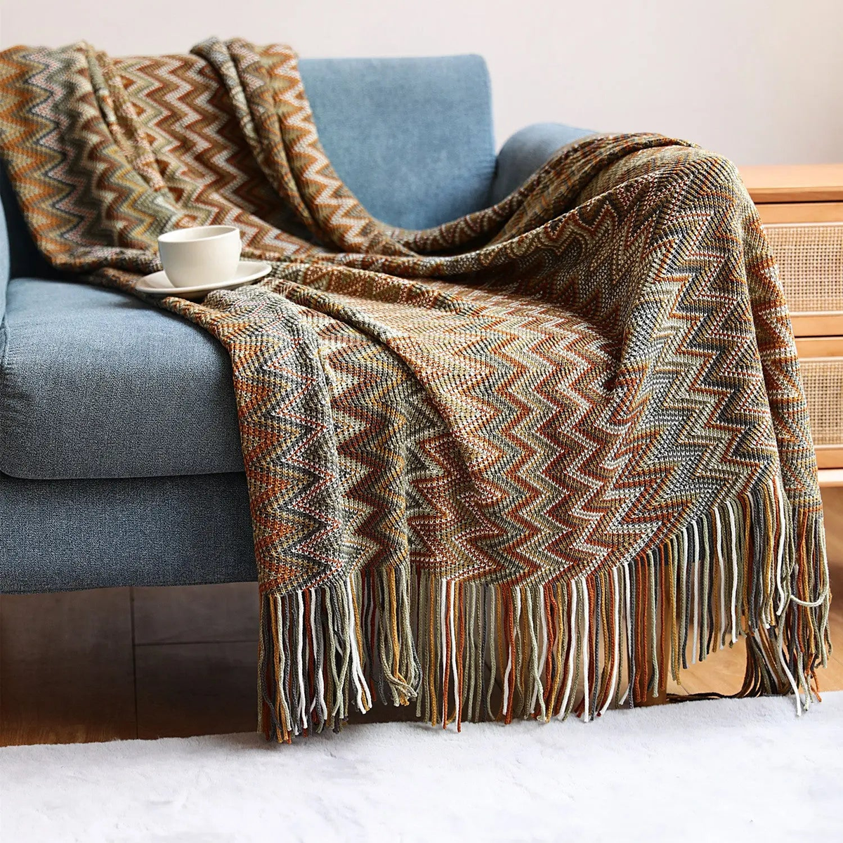 A brown chevron throw with rust, tan and cream zigzags spread across a blue couch, the fringe hanging over a white rug.