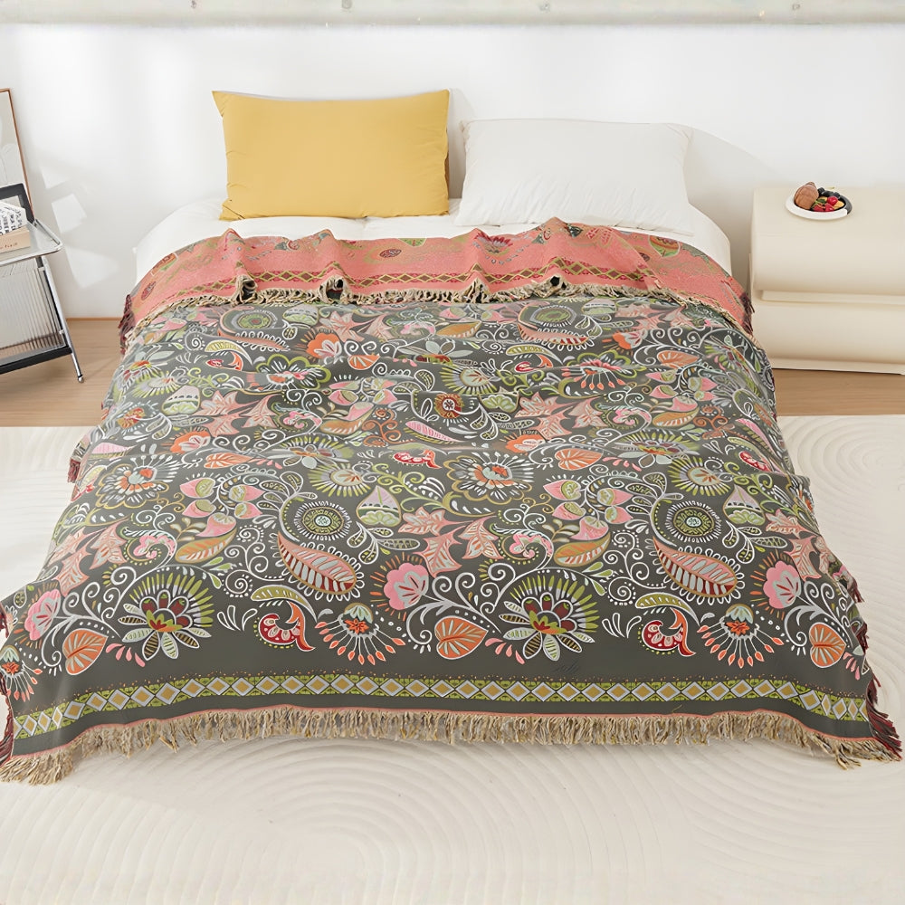 A charcoal throw blanket with pink, coral and white leaves and paisleys over a white bed, the top turned back to show its coral pink reverse