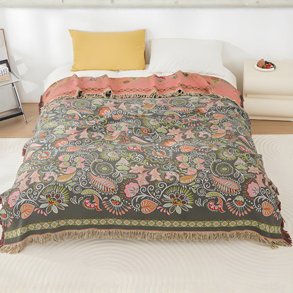 A charcoal throw blanket with pink, coral and white leaves and paisleys over a white bed, the top turned back to show its coral pink reverse