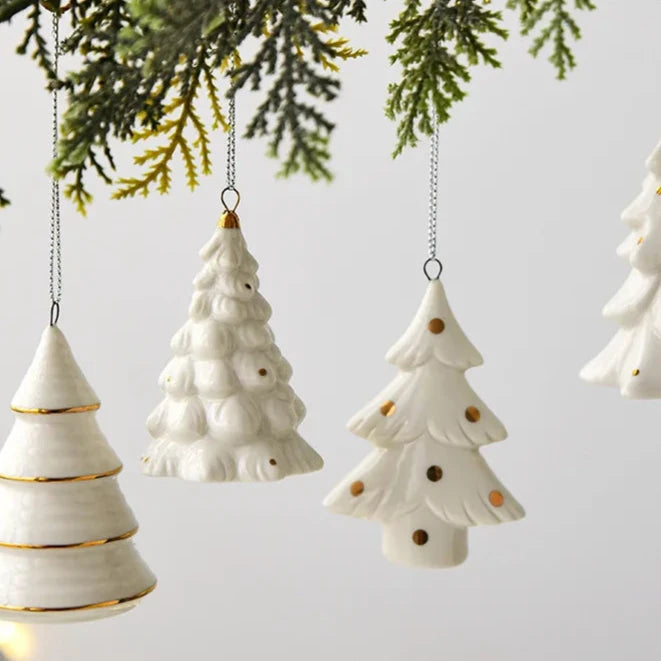 Three white ceramic tree ornaments with gold details hanging in a row from evergreen branches