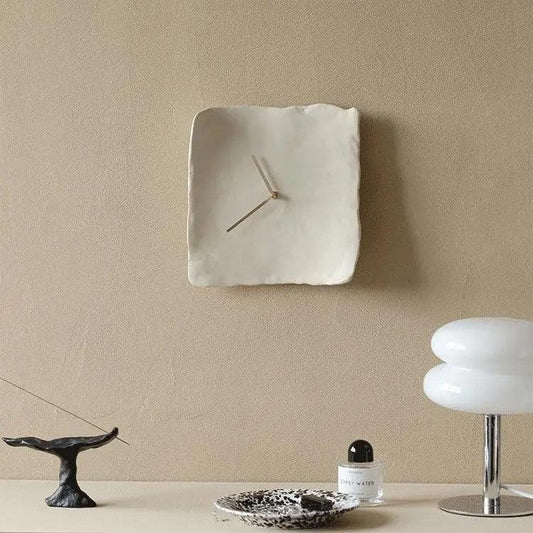White crumpled resin wall clock on a beige wall above a desk with a white table lamp