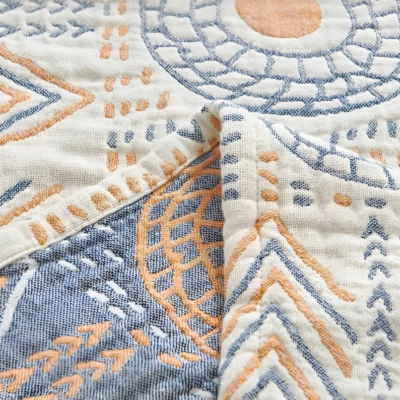 Close-up of a folded corner showing the cream face and the slate blue reverse of the woven cotton blanket, with its narrow hemmed edge