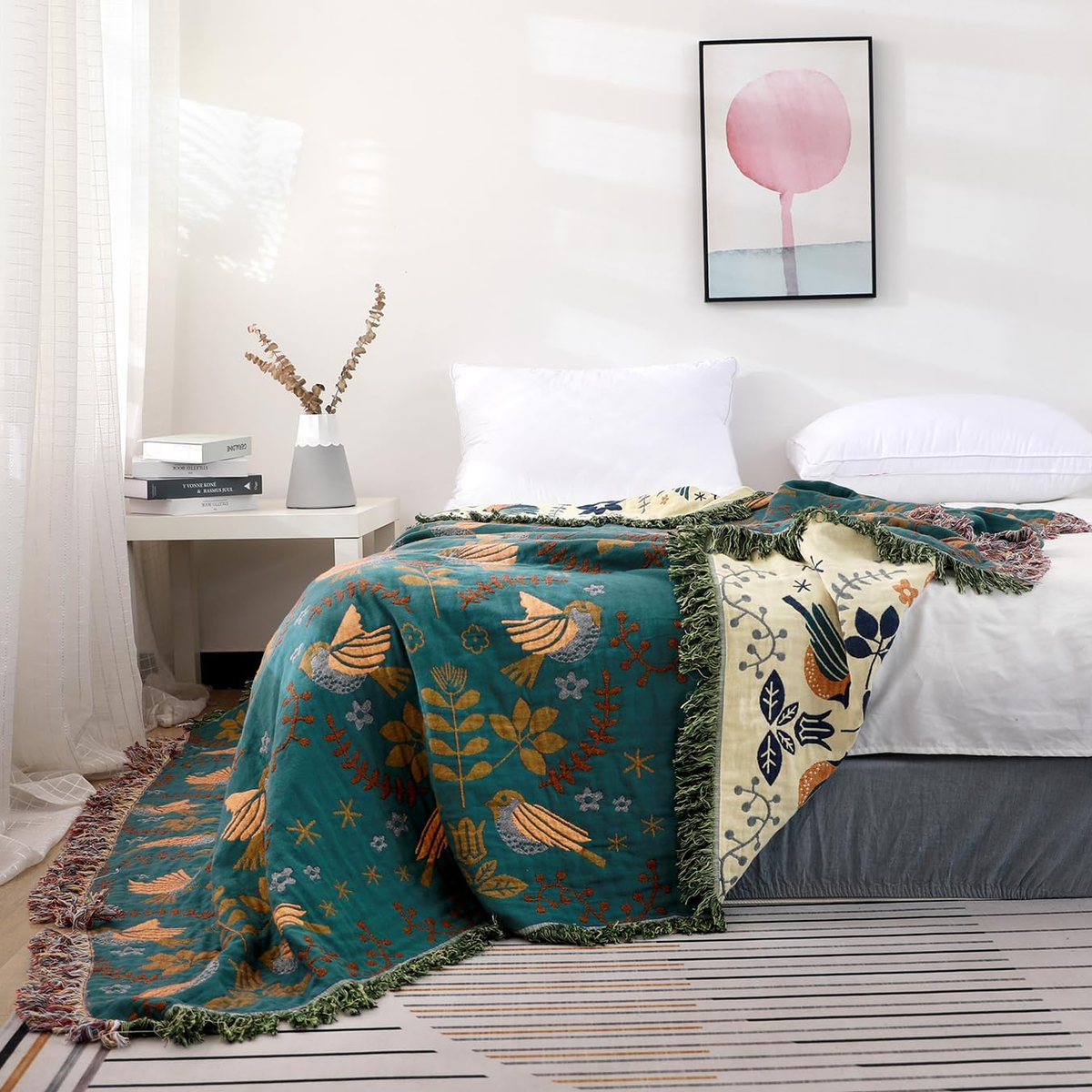 The teal bird throw falling from the foot of a bed to the floor, with its cream side turned over across the mattress