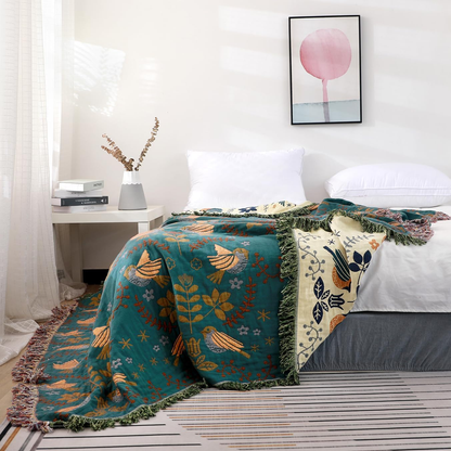 The teal bird throw falling from the foot of a bed to the floor, with its cream side turned over across the mattress