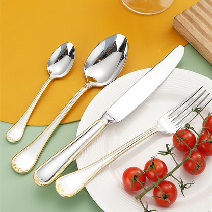 Gold trim knife, fork and spoons beside a white plate with cherry tomatoes
