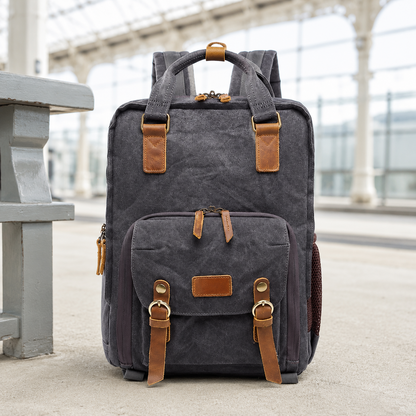 Charcoal gray waxed canvas camera backpack on a bright station platform.