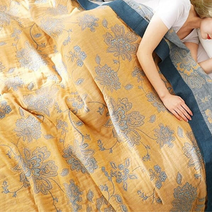 Woman resting under the mustard floral blanket, the folded corner showing the blue border and the patterned reverse side