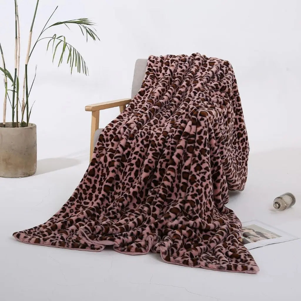 A pink leopard print throw blanket with dark brown spots on a dusty pink ground, draped over a wooden armchair.
