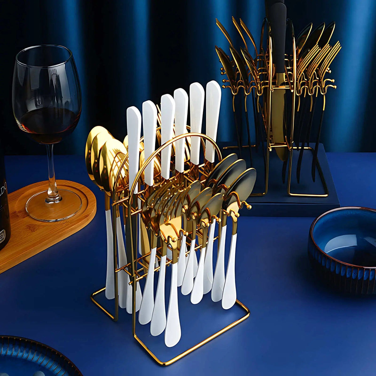 White and gold cutlery set on its gold arched rack in front of a black and gold set on a blue dining table