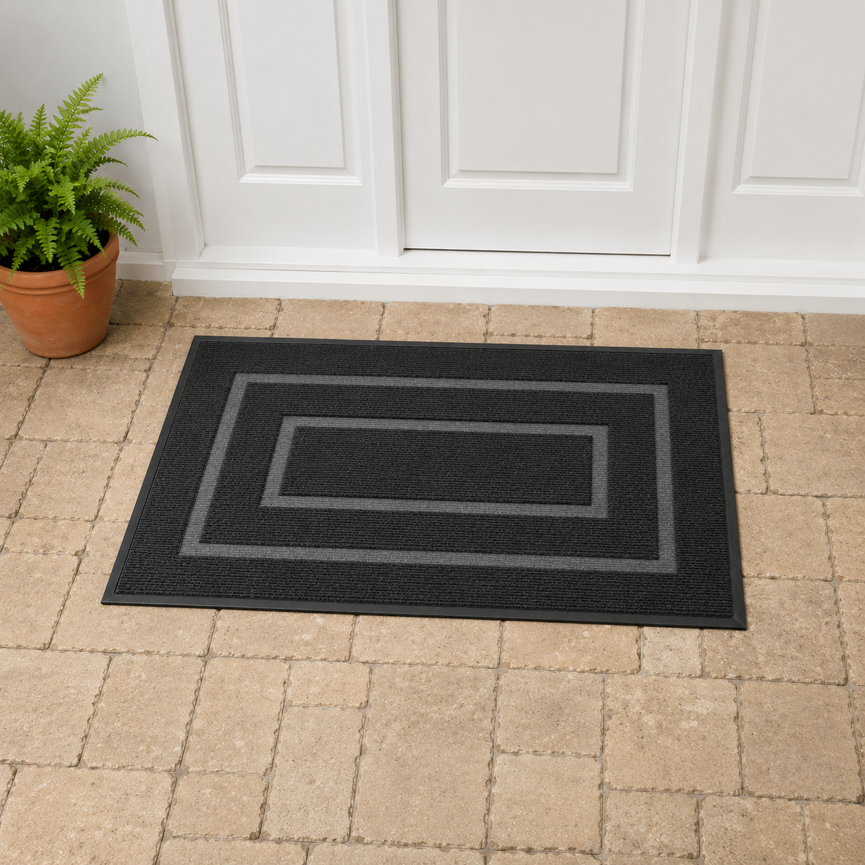Black door mat with two pale gray bands around a plain center panel, lying on stone paving in front of a white front door.