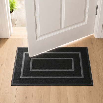 Black door mat on oak floorboards with a white door swinging open above it, showing the gap between the door and the mat.